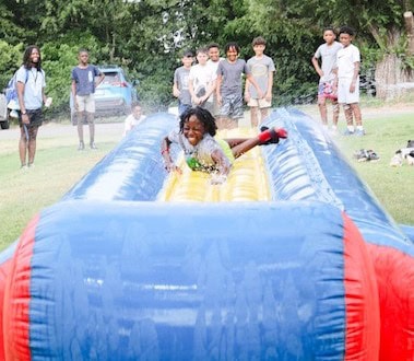 Children at a summer camp participate in outdoor activities like ziplining and kayaking to build confidence and social skills.